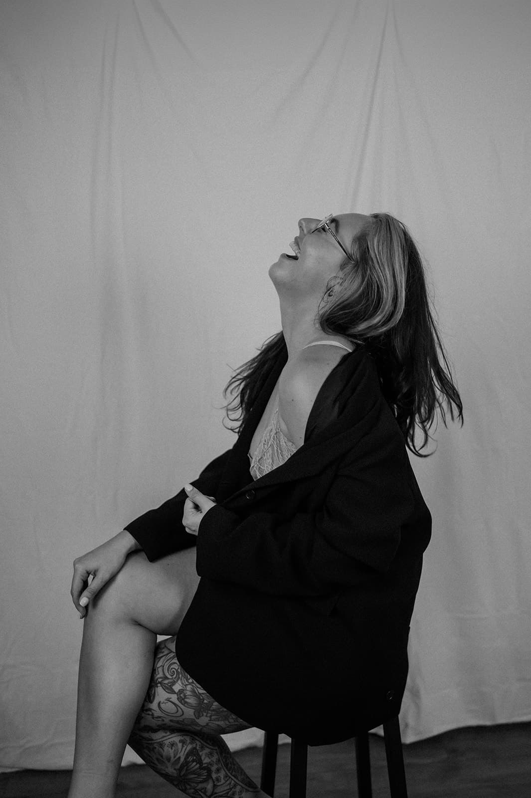 Nicole, wearing glasses and a black 'The Women's Wellbeing Club' t-shirt, sits on a dark grey couch working on a laptop.